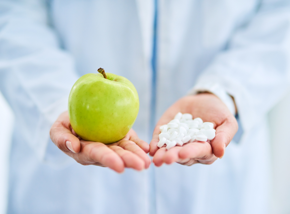 Closeup shot of an unidentifiable doctor holding an apple and a variety of pills in her hands