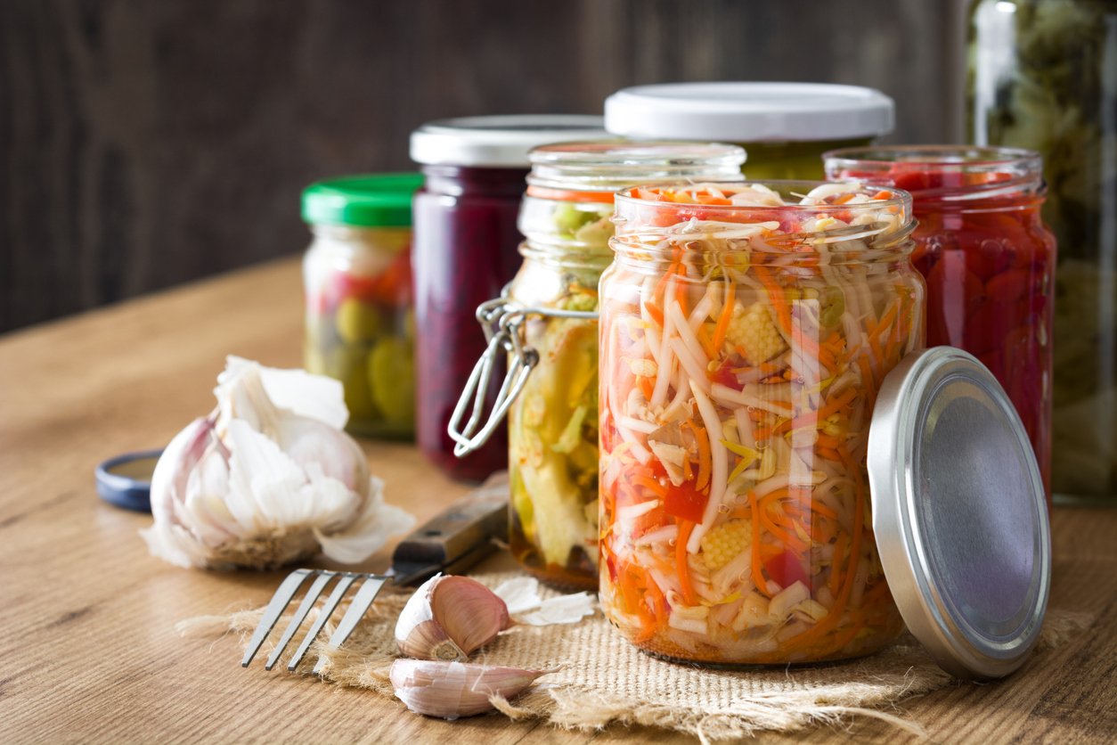 Fermented preserved vegetables in jar on wooden table.