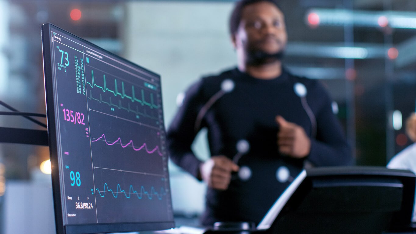 close-up shot of a monitor with ekg data male athlete runs on a treadmill with gm