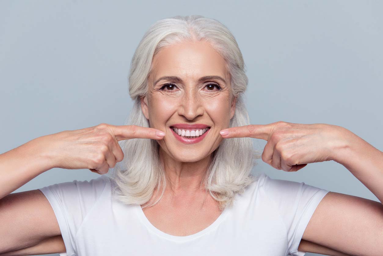 elderly woman pointing to own smiling teeth