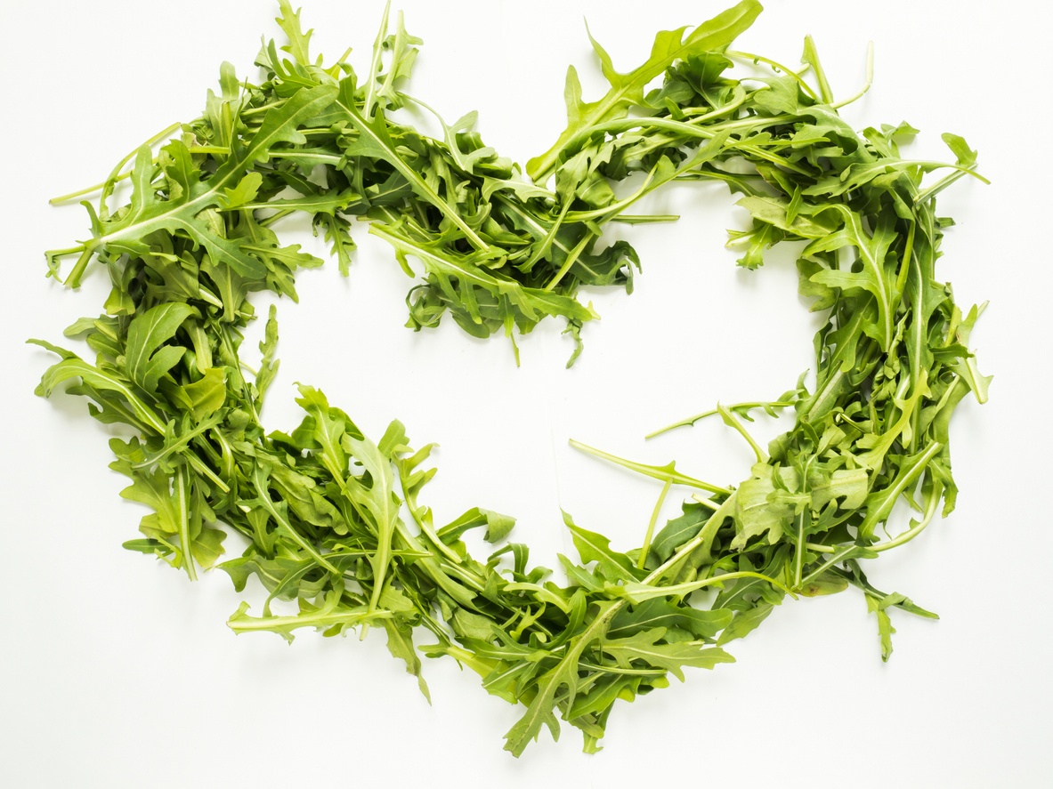 Green leaves of arugula laid out in the shape of heart on white background.