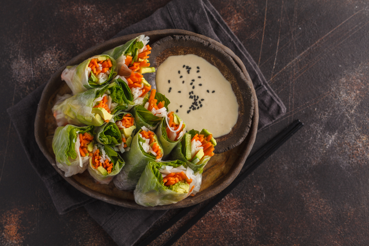 Fresh handmade vegan asian spring rolls with rice noodles, avocado, carrots and tahini dressing on black dish