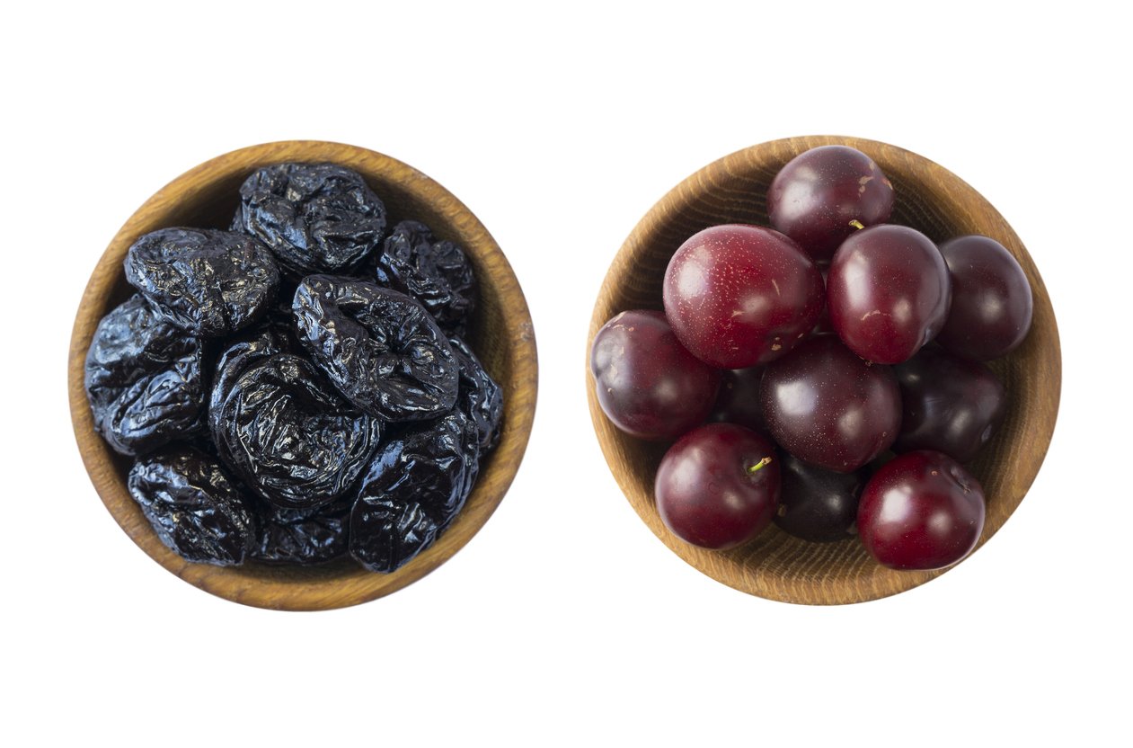 Fresh plums and dried prunes isolated on a white background. Dried prunes and fresh plums in a bowl on white background. Dried prunes and plums with copy space for text. Top view.