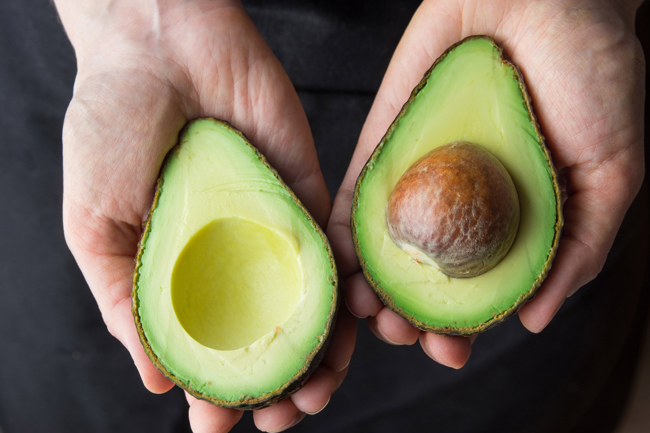 Un aguacate cortado por la mitad en las manos