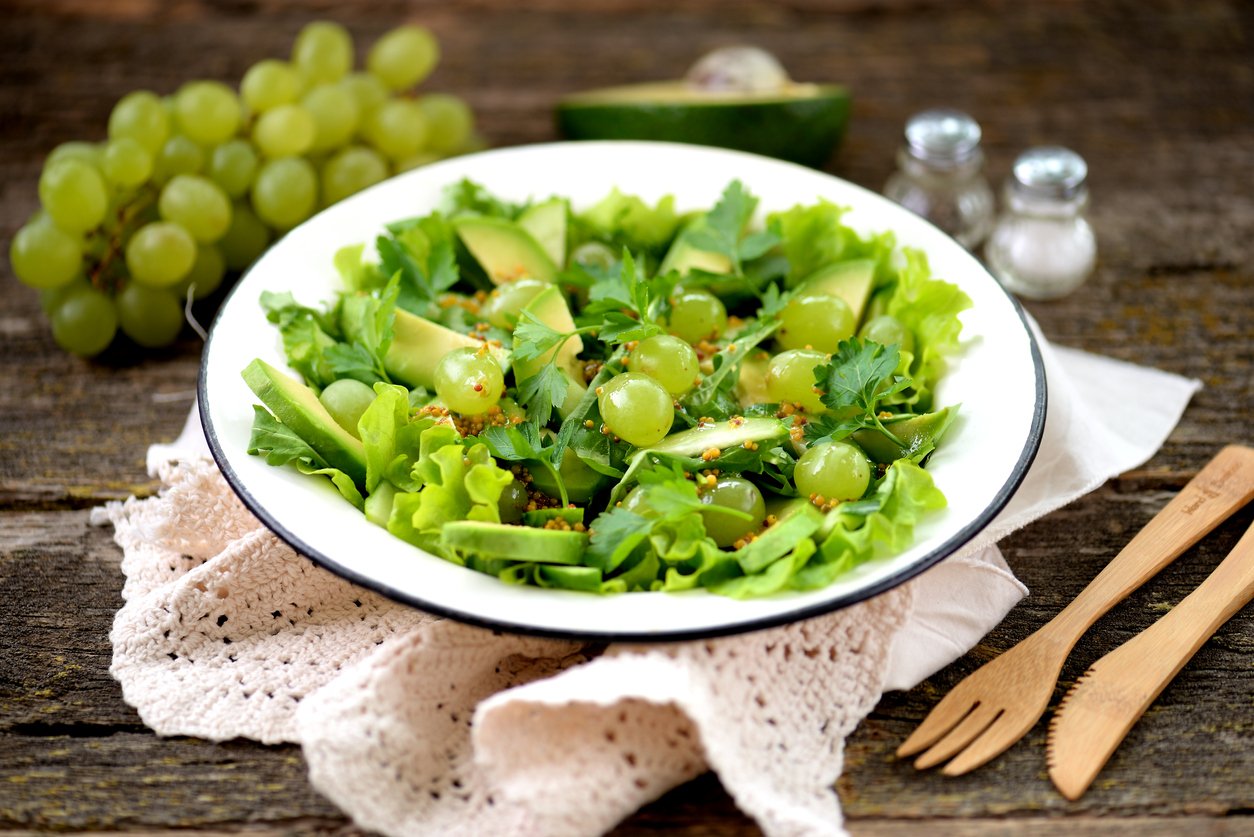 Healthy green salad from avocado, cucumber, grapes, parsley and lettuce with olive oil dressing, balsamic vinegar and grain mustard.