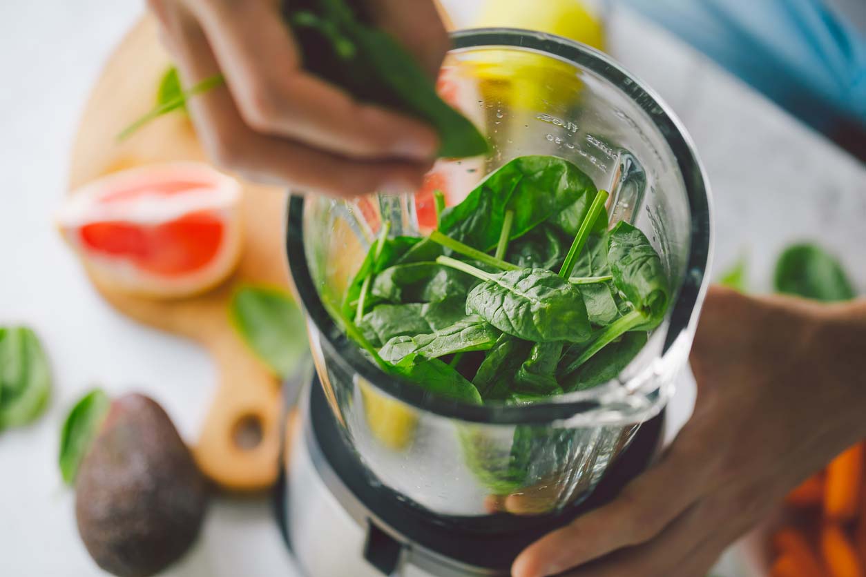 hand putting spinach in personal blender