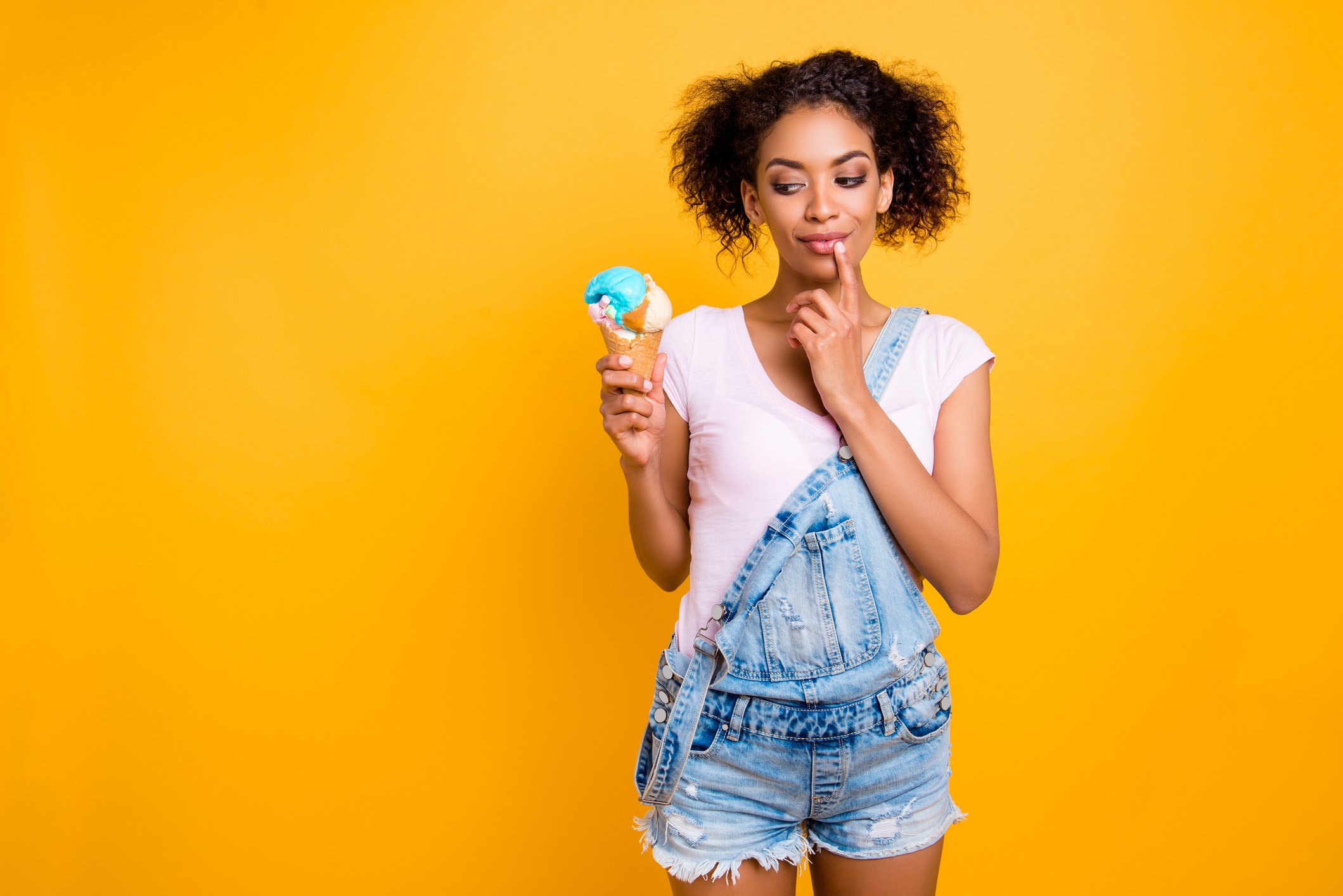 A young woman holds an ice cream cone on a yellow background