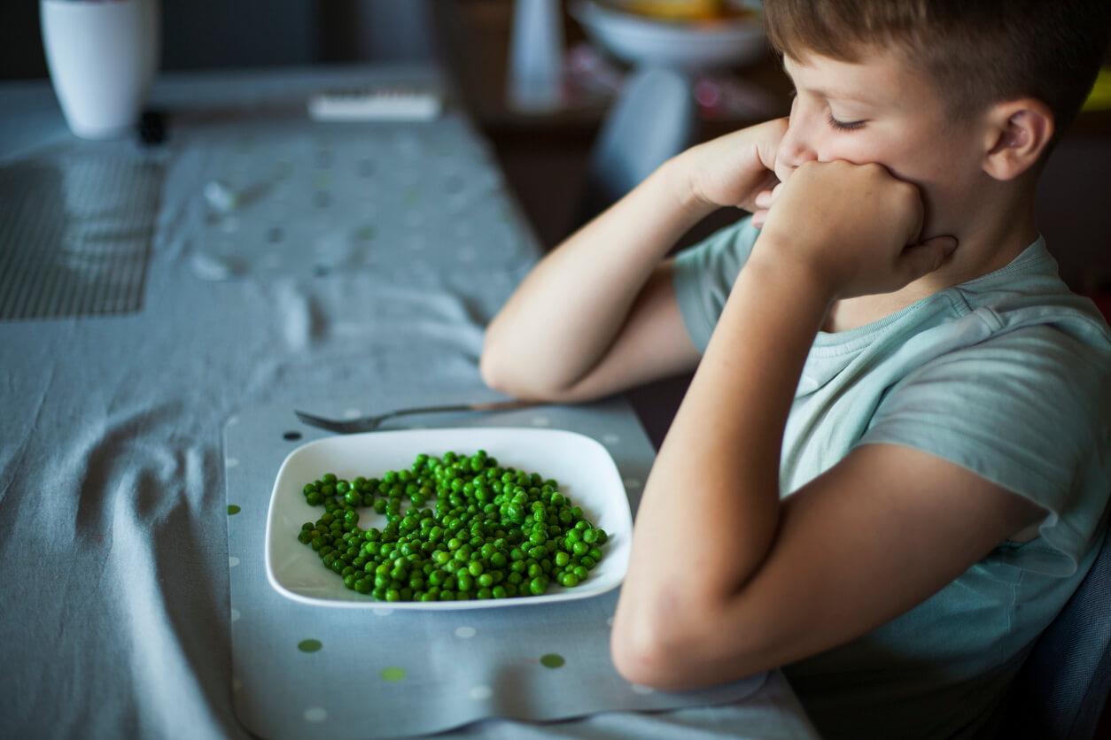 boy sitting in front of a plate of green peas