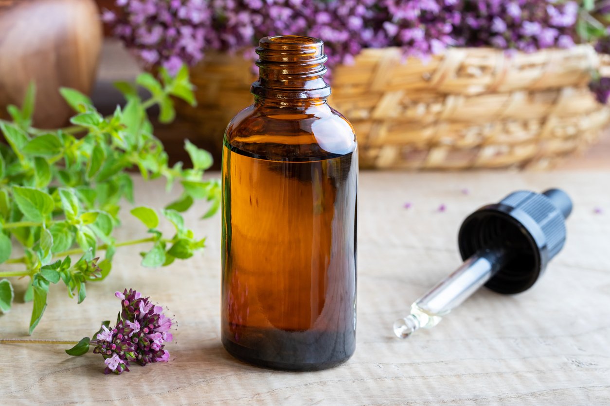 A bottle of oregano essential oil with fresh blooming oregano