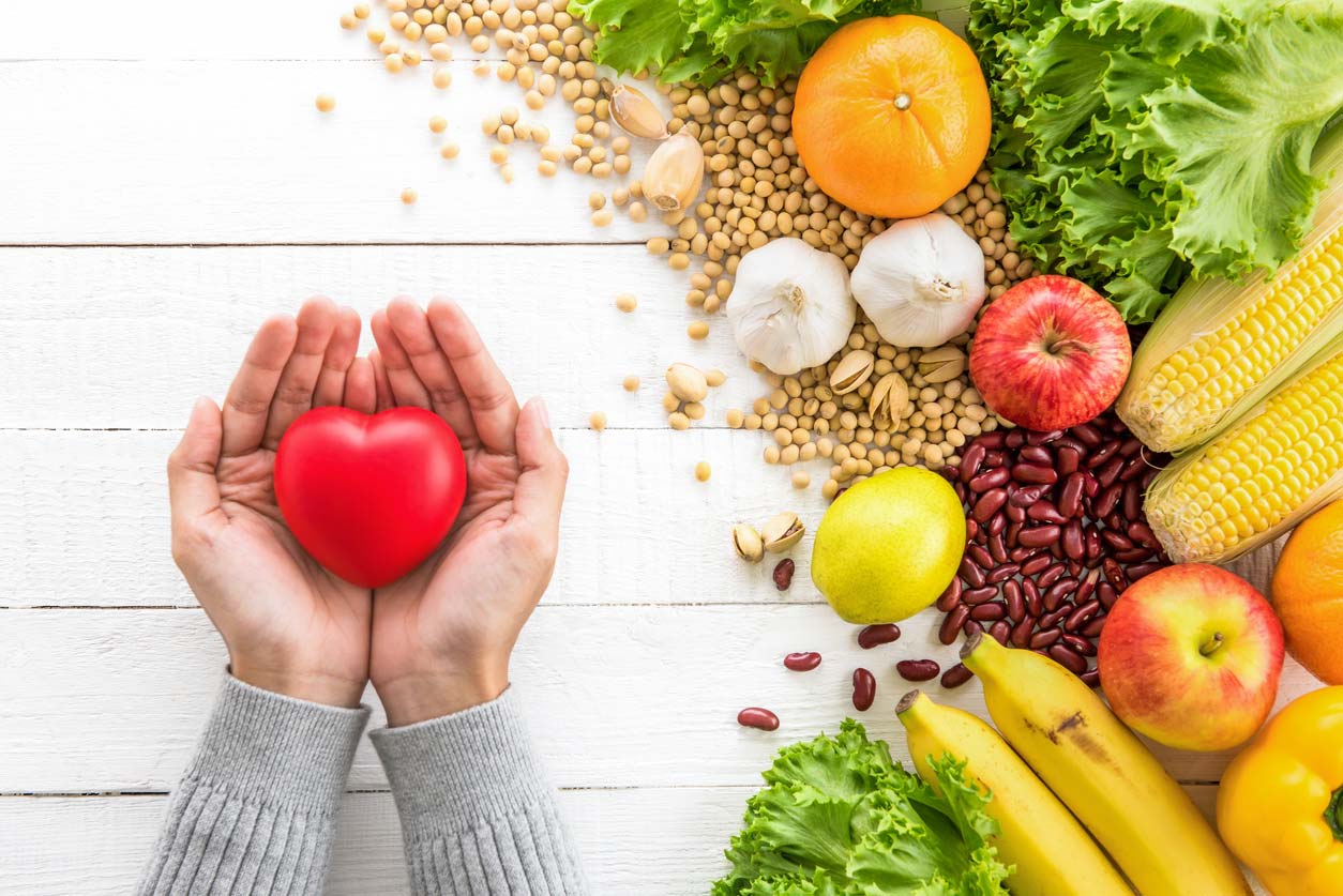 hands holding heart next to healthy foods on table